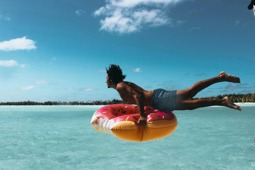 Man jumping into turquoise water with a donut float in French Polynesia.