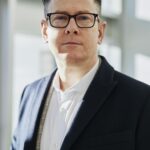 Profile portrait of a confident business executive wearing eyeglasses in a sunlit office setting.